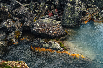 Scenic nature background of turquoise clear water stream among rocks with mosses and lichens. Atmospheric mountain landscape with mossy stones in transparent mountain creek. Beautiful mountain stream.