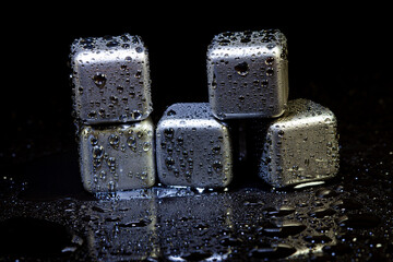 Stainless steel cubes simulating ice for cooling drinks on a black surface with a reflection.