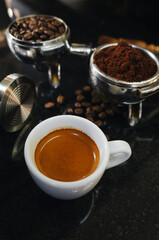 Obraz na płótnie Canvas A portafilter with coffee beans, a portafilter with ground coffee, an espresso shot on black table.