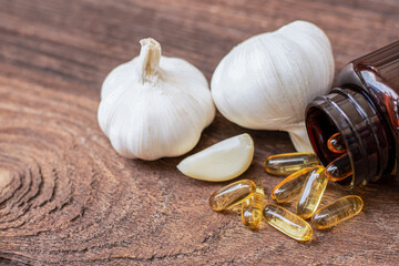 Garlic oil capsule gel and fresh garlic bulb isolated on wood table background.