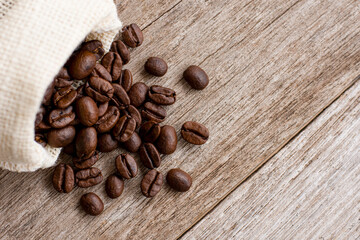 Roasted coffee beans in hemp sack bag isolated on wood table background. Top view. Flat lay.