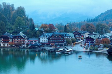 Fototapeta na wymiar Sightseeing boats cruising on Konigssee ( King's Lake ) with lakeside hotels, resorts and boathouses at foggy misty dusk ~ Beautiful fall scenery of Bavarian countryside in Berchtesgaden Germany