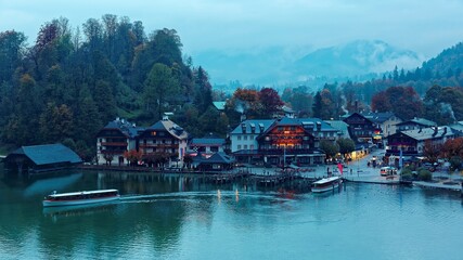 Sightseeing boats cruising on Konigssee ( King's Lake ) with lakeside hotels, resorts and boathouses at foggy misty dusk ~ Beautiful fall scenery of Bavarian countryside in Berchtesgaden Germany