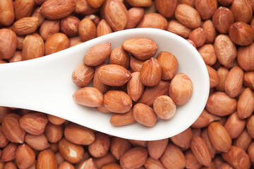 Macro Close up of organic red brown peanuts (Arachis hypogaea) on a white ceramic soup spoon. Top view