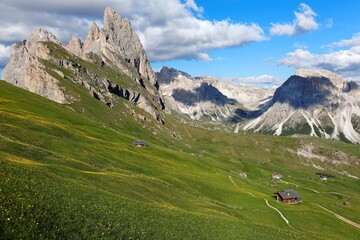 Fototapeta na wymiar Beautiful scenery of Dolomites on a sunny summer day with view of majestic Odle (Geisler) mountain peaks in background & wooden huts on grassy hills at Seceda, Val Gardena, South Tyrol, Italy, Europe