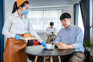 Obraz premium Asian woman waitress serving coffee and bread to client while wearing face mask and face shield