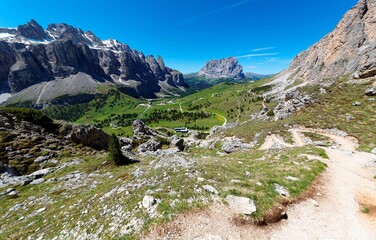 Scenery of Gardena Pass on a sunny summer day with rugged Sella & Sassolungo mountains in background, highways & hiking trails winding through the green grassy valley in Dolomites, South Tyrol, Italy