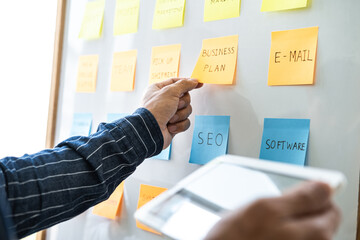 Young creative business people use post it notes sticky note on board to share idea, Analysis data chart and graph with planning strategy thinking in office