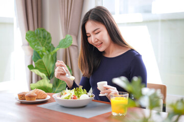 Young asian woman use a salad dressings spoon to mixing with fresh vegetable and drinking orange juice