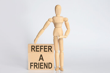 Wooden man shows with a hand text REFER A FRIEND concept on the wooden block