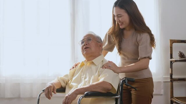 Asian happy disabled elderly in wheelchair with daughter and granddaughter smiling playing together in living room at home, family visit to support old senior man
