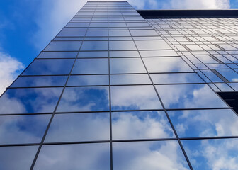 View of a modern glass skyscraper. Reflection of a cloudy blue sky in a glass skyscraper