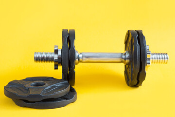 Dumbbell with disks on a yellow background close-up. Sports lifestyle, strength training, gym. Copy space