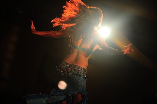Silhouette view of a solo belly dancer dancing in the dark