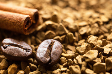 Beans of natural roasted coffee and a cinnamon stick close-up lie on the granules of instant...