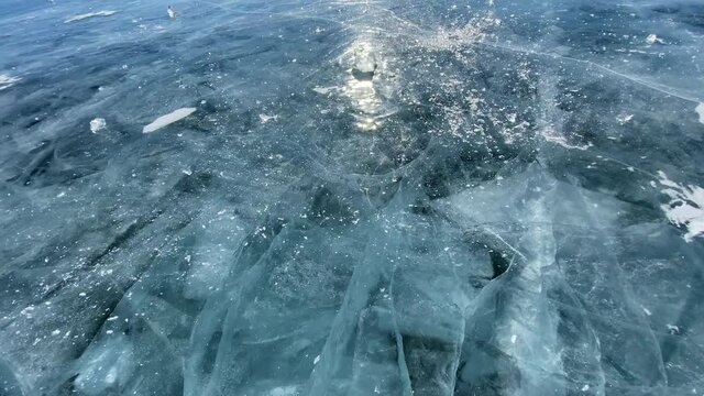 The guy breaks a piece of ice smooth transparent blue ice of frozen Lake Baikal. The ice floe breaks into many fragments. Beautiful ice with deep cracks.