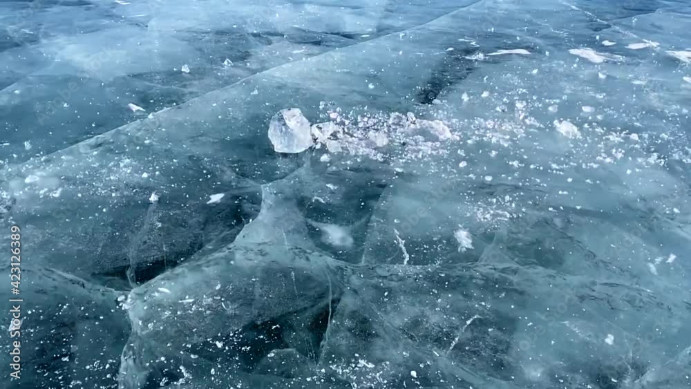 Wall mural Slow motion video - a guy breaks a piece of ice on the smooth transparent blue ice of frozen Lake Baikal. The ice floe breaks into many fragments. Beautiful ice with deep cracks.