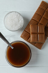 Caramel sauce, bar and salt on white wooden background