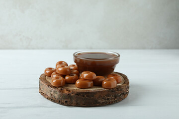 Board with caramel sauce and candies on white wooden table