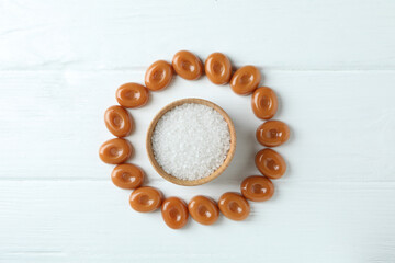 Caramel candies and bowl of salt on white wooden background