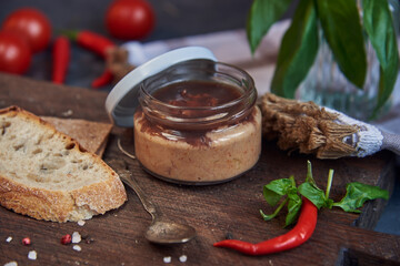 Handmade chicken pate in a glass jar on a wooden board .