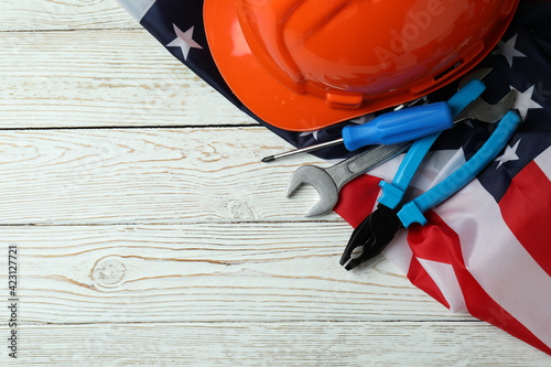 American flag, hard hat and tools on white wooden background