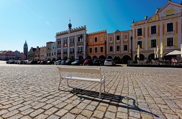 An empty bench in Telc ( Teltsch ) Old Town Square under blue clear sky with historic houses of colorful renaissance & baroque facade, a beautiful UNESCO site in Czech Republic, Europe