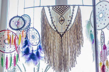 Macrame panels in natural colors and dream catchers on the background of the window. Weaving of threads, knots and braids macrame, hanging on the wall, and dream catchers