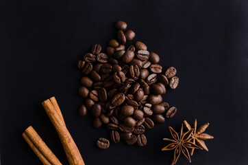 plenty of coffee beans with hot spices for the aroma and taste of the drink on a black background.