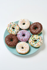 Party desserts. Freshly baked various delicious colourful round glazed donuts with sprinkles on the plate over white background