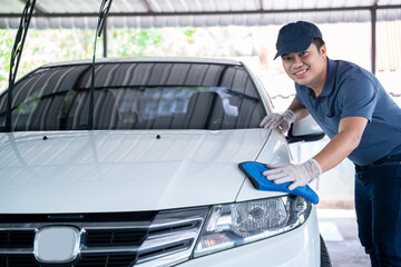 happy asian man in uniform holds the microfiber in hand and polishes the car, Car wash service...