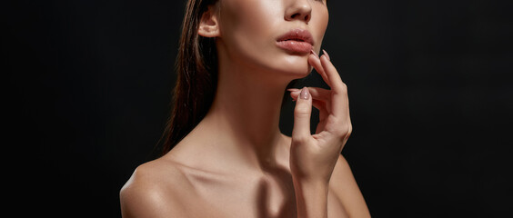 Cropped portrait of delicate brunette woman with pouty lips and professional makeup posing isolated over black background