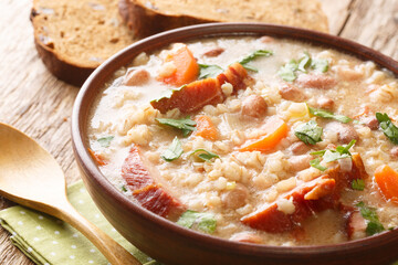 Thick rich barley and bean soup with smoked meat and vegetables close-up in a bowl on the table. horizontal