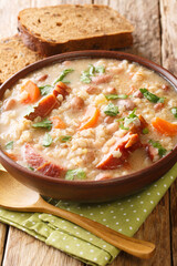 Ricet barley and bean soup with smoked meat and vegetables close-up in a bowl on the table. vertical