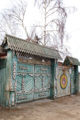 Old Traditional Russian Rustic Gate Fence with Wooden Carvings Ornaments and Weathered Paint against Bare Birch Tree