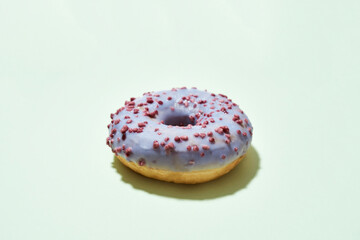 Dessert that will melt in your mouth. Freshly baked delicious donut with colorful sprinkles and purple sugar glaze isolated on light background