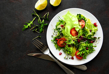 Fresh green mixed  salad bowl with tomatoes and microgreens  on black concrete background. Healthy food, top view.