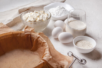 Ingredients for making Basque Spanish burnt Saint Sebastian cheesecake. Cream cheese, sugar, eggs, flour, cream, baking dish covered with paper. Recipe step by step flat lay top view