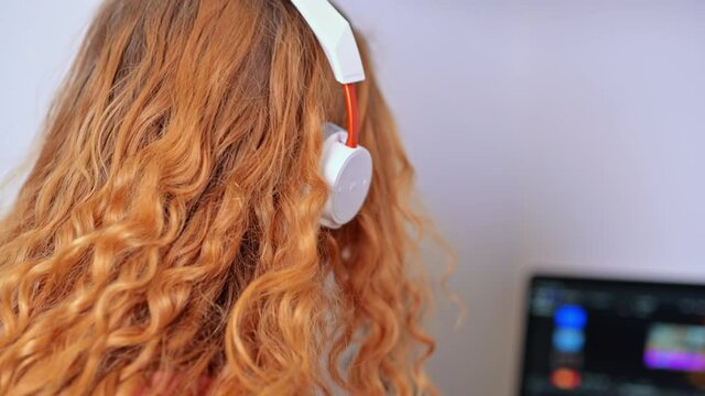 Young content creator girl editing video on her laptop with headphones. Microphone and camera lens on table. Working from home