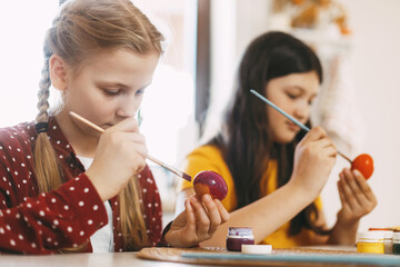 Two sisters are sitting at the table and painting Easter eggs in different colors for Easter