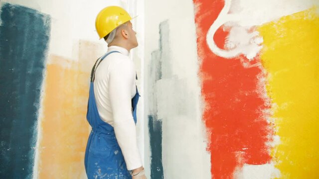 Professional painter in white turtleneck painting the wall with a roller and giving a thumbs up