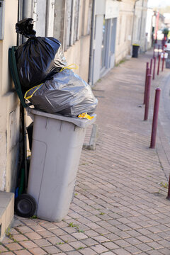 Rolling trash can overflowing bag grey wheelie in street city