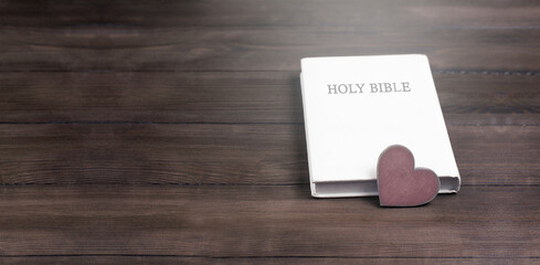 Closed white book Holy Bible. Heart on the book. On a wooden table.