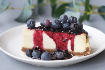 Portion of cheesecake with blueberry jam and fresh blueberries on plate. Sweet delicious homemade cake.