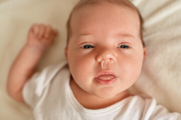 Newborn boy or girl having runny nose and snot, infant wearing white bodysuit or t shirt looking...