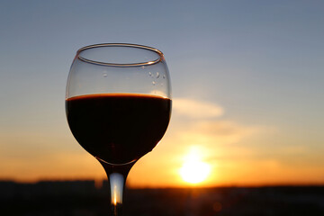 Glass with red wine on beautiful sunset background. Concept of celebration, evening party at resort, romantic dinner outdoors