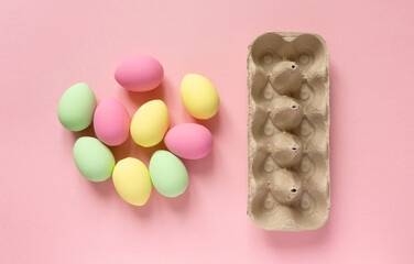 Fototapeta na wymiar Easter eggs painted in pastel colors with cardboard box on pink background, top view