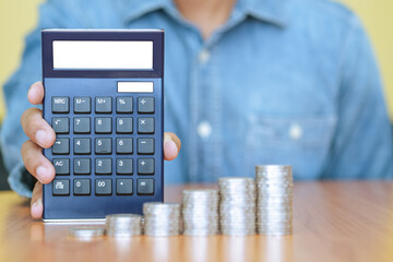 A businessman with a calculator and a stack of coins in foreground. Business, finance and growth concept