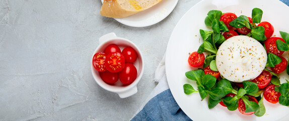 Delicious salad with sliced tomatoes and burrata on light gray background.