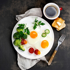 Fried eggs with vegetables on dark grey background